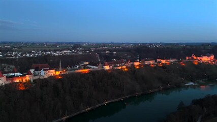 Nighttime drone shot of the lit Burghausen Castle in Bavaria, Germany. View from Woehrsee Lake with reflections on the water and city lights. Luftaufnahme Burg zu Burghausen nachts beleuchtet