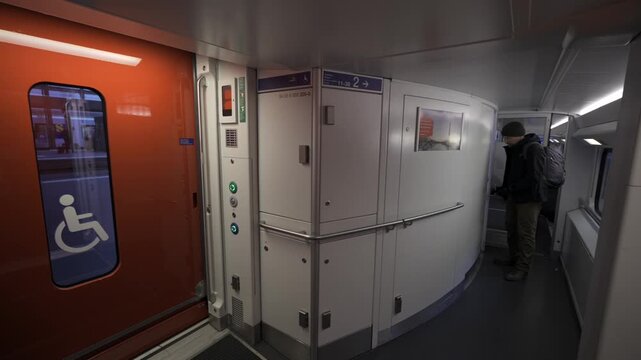 A passenger exits the restroom aboard a stationary Swiss double-decker train at a platform stop. The modern interior reflects accessibility, comfort, and efficient European public transport design. 