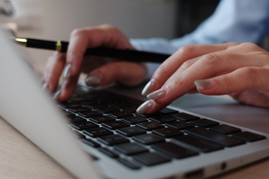 Businesswoman typing on laptop keyboard and holding pen