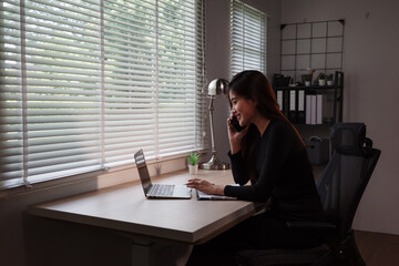 Asian businesswoman talking on phone and working on laptop in home office