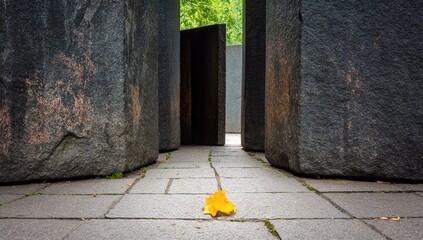 A solitary yellow leaf rests on a paved path amidst large, dark gray stone blocks, creating a contemplative atmosphere.