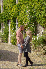 Fototapeta premium A loving couple holds hands on a cobblestone street in the romantic medieval village of Pérouges, France. A perfect concept for love, travel, and relationships.