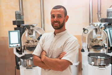 Roasting workshop, a worker smile standing near roasting machines. The atmosphere is vibrant, highlighting the detailed preparation of coffee blends