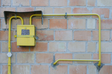Yellow metal pipe and gas meter on a brick wall with copy space for text.
