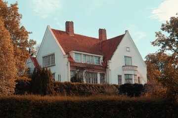Obraz premium Charming white house with red roof surrounded by lush greenery on a bright day in the countryside, showcasing classic architectural style and serene atmosphere
