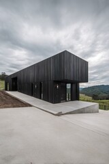 Obraz premium Modern black building stands on a hillside with panoramic views over vineyards under an overcast sky during early evening hours