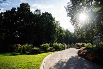 Obraz premium Scenic sunlit garden path with vibrant flowers in Lancut, Poland