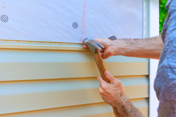 Obraz premium Worker is using hammer to secure new PVC vinyl siding while working on home renovation project outside.