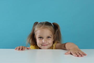 Curious little girl peeking over white table against light blue background