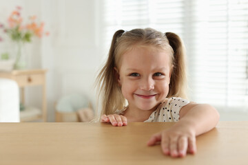 Curious little girl peeking over wooden table indoors, space for text