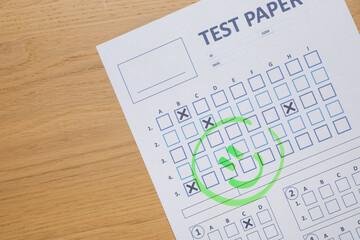 Answer sheet with drawn happy face on wooden table, top view. Student passing exam
