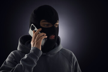 Criminal in mask talking on phone against dark background. Space for text