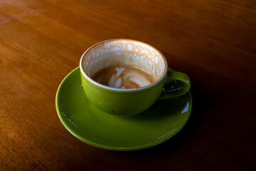 An empty green coffee cup with leftover foam from a latte sits on a matching saucer on a polished wooden table.