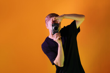 Man with camera taking photo in neon lights against orange background. Space for text