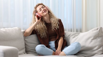 Obraz premium Happy woman listening to music in headphones on sofa at home