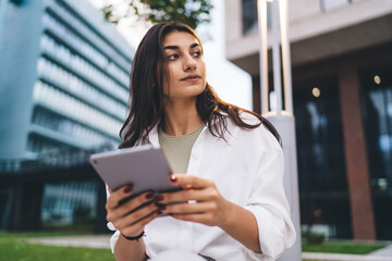 Thoughtful young woman holds digital tablet, symbolizing focus, digital research, remote productivity and modern tech-centered thinking in connected lifestyle.