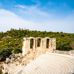 Obraz premium Ancient theatre ruins, with arches and tiered seating, overlook a lush hillside under a vibrant sky.