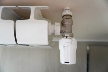 Close-Up of a White Thermostatic Radiator Valve with Temperature Control Dial Attached to Wall-Mounted Radiator for Central Heating System, Energy Efficiency, and Climate Regulation Concept