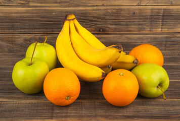 Green apples, oranges and bananas on a wooden background.