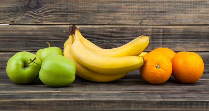 Green apples, oranges and bananas on a wooden background.