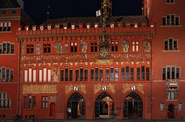 Photo of the ornately decorated facade of the red town hall in Basel, illuminated at night