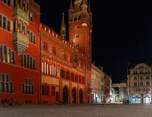 Photo of the ornately decorated facade of the red town hall in Basel, illuminated at night