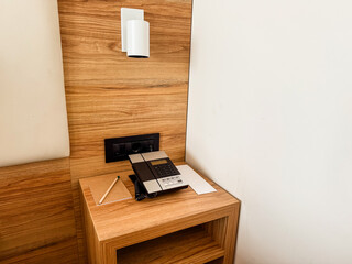 Bedside table with telephone, lamp, and notepad in hotel room. Communication, service, and assistance concept in hospitality environment for guest comfort.