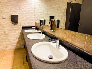 Triple sink counter with mirror and tiled wall in modern restroom. Cleanliness, hygiene, and functional hospitality facility for comfort, order, and guest service.