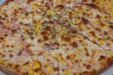 Ham pizza with corn on a white plate.
