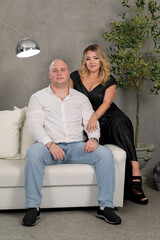 Obraz premium loving couple in the room on a white sofa against a gray wall. husband and wife. groom and bride