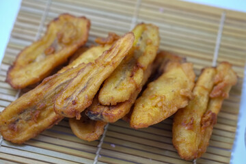 A close-up shot of several pieces of fried bananas, golden brown and glistening with oil, on a bamboo mat.