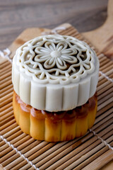 Two mooncakes, one light-colored and one golden-brown, are stacked on a woven bamboo mat. The top mooncake has a detailed floral design.