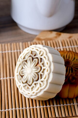  A close-up shot of two mooncakes on a bamboo mat, with a white teapot and a teacup blurred in the...