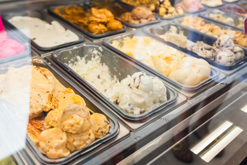 A close-up and appetizing view of a variety of brightly colored gelato flavors displayed in metal trays behind a glass case, showcasing a selection of creamy, frozen desserts ready to be served.