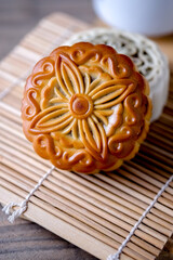 Traditional mooncake with intricate floral pattern placed on bamboo mat, symbolizing Mid Autumn Festival celebration and Asian pastry culture.