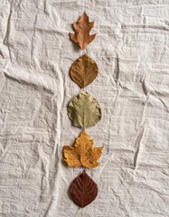 Fototapeta premium Colorful Autumn Leaves Arranged Vertically on Wrinkled Grey Linen Fabric Close Up