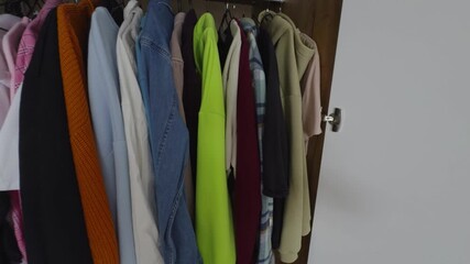 A first-person perspective POV video shows a man's hands opening a modern, light-colored wardrobe. The camera, positioned over the shoulder, captures his hand reaching into the organized closet