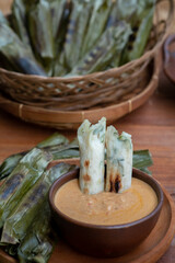 reshly grilled otak-otak made from mackerel fish, wrapped in banana leaves, served with a creamy spicy-sweet peanut sauce in a rustic woven basket.