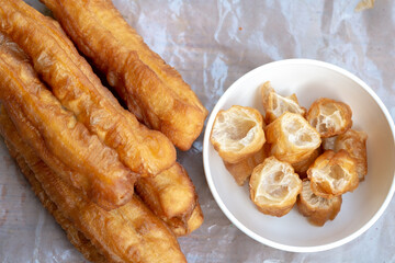 A close-up, top-down view of Youtiao, also known as Chinese fried dough sticks or Cakwe in Southeast Asia, with some pieces cut up and served in a white bowl. These crispy, airy golden-brown delights 