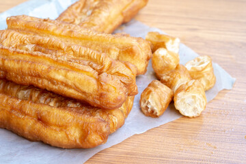 Long golden fried dough sticks lying on paper with smaller cut pieces scattered nearby, showing their crisp shell and soft airy inside on a wooden table.