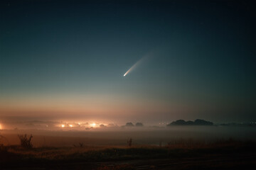 A spectacular comet shines brightly above foggy rural farmlands, casting a cinematic atmosphere across the fields at dawn as the first light of day begins to emerge