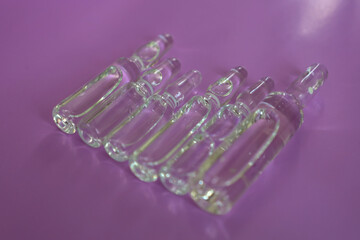 Several transparent glass ampoules with a medical solution are arranged in a neat row on a vibrant magenta background. The composition symbolizes modern medicine, pharmaceuticals, and scientific resea