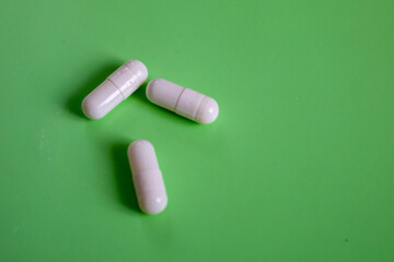 Three white capsules are placed on a clean green background, creating a simple but expressive composition. The image is ideal for visualizing concepts related to health, treatment, and the pharmaceuti