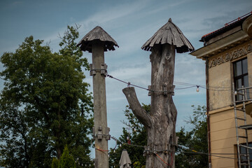 Two tall wooden poles with conical thatched tops and string lights attached, set beside an old building and trees.
