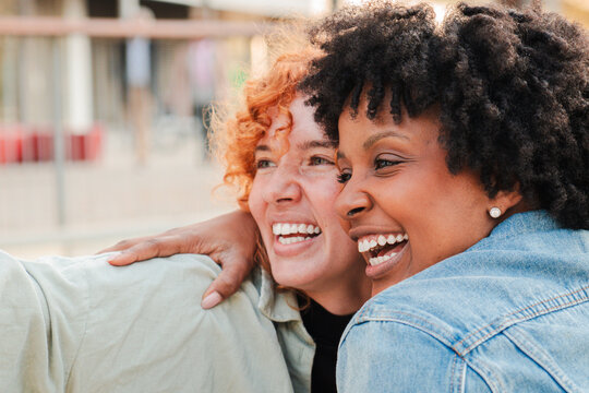 Two cheerful friends are smiling broadly as they embrace each other, capturing a joyful moment with a selfie, showcasing the warmth and happiness of their friendship in a delightful interaction.