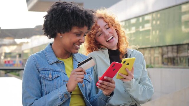 Two cheerful girls are engaging with their mobile phones, making a purchase using a credit card, and enjoying a delightful shopping experience together while sharing smiles and excitement.