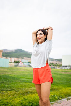An attractive woman between 40 and 50 years old is exercising on a cloudy day outdoors.The woman stretches her arms upwards.Concept of adult women doing sports.
