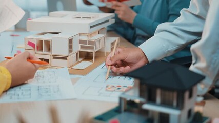 This image showcases a collaborative workspace where hands are engaged in architectural model design, surrounded by blueprints and 3D house models, highlighting creativity and teamwork. SACTR