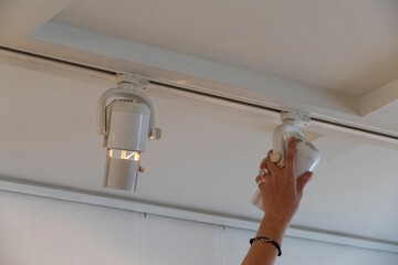 Female hand adjusting directional spotlight in art gallery ceiling for precise painting illumination, professional lighting setup for exhibitions, museums, and interior design