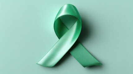Satin green awareness ribbon symbolizing mental health, organ donation, or other causes, laid flat on a mint-colored background.